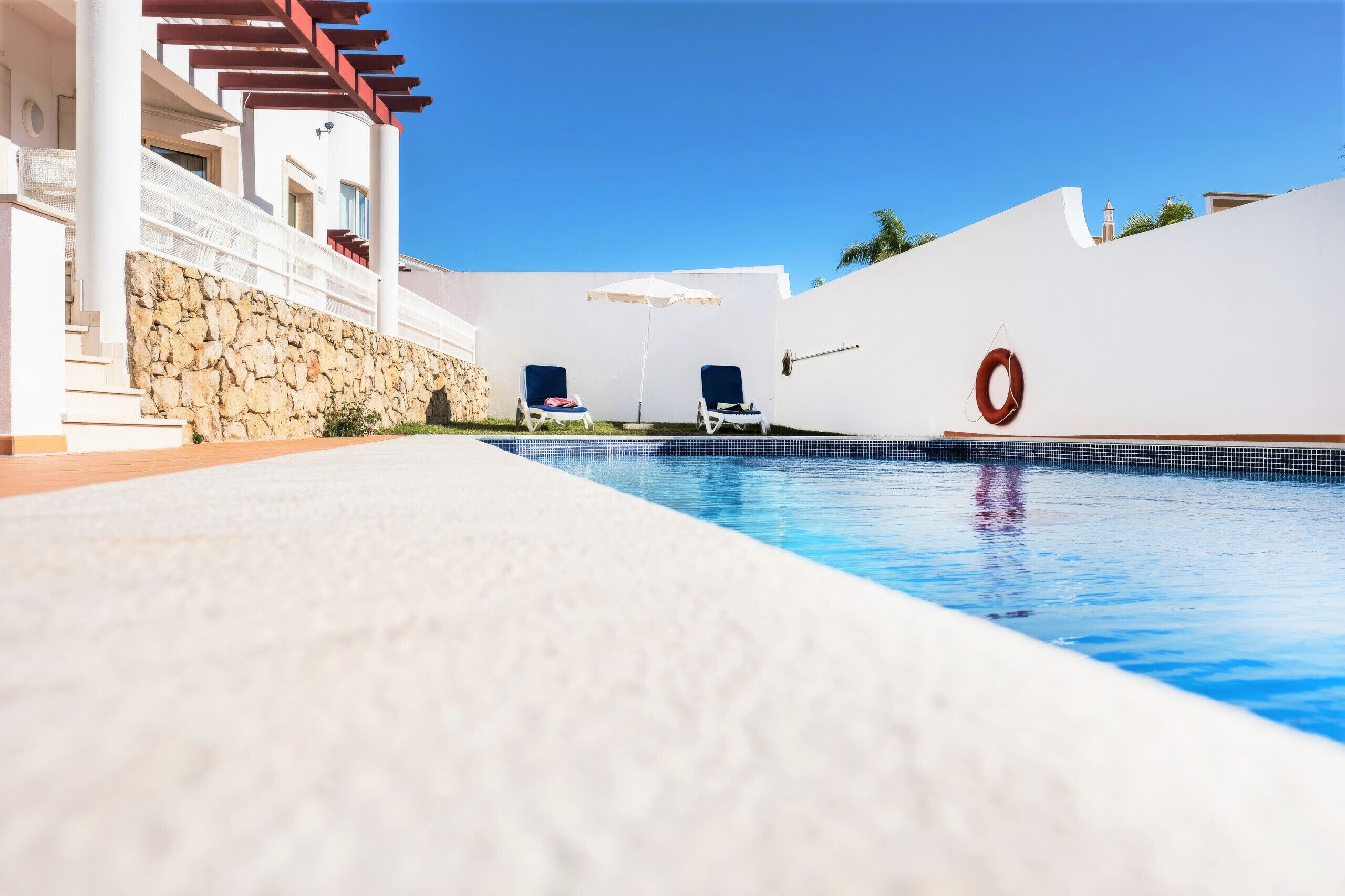 Una piscina con lettini e un galleggiante, circondata da un edificio bianco con pareti in pietra.