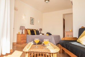 Ein Hotelzimmer mit Bett, Nachttisch, Lampe sowie einem Tisch mit Getränken und einem Buch.