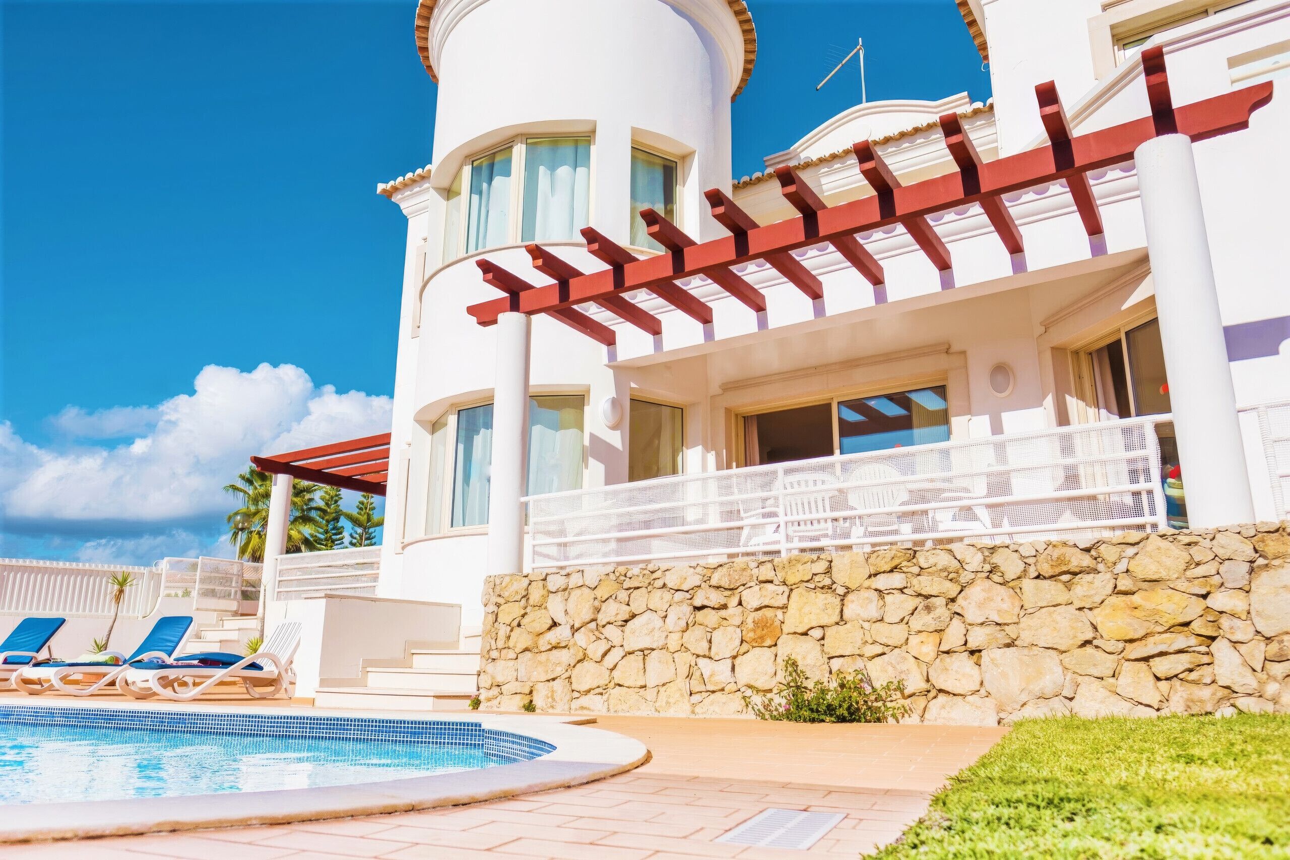 A resort with a swimming pool, lounge chairs, and a stone wall.