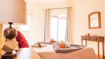 A hotel room with a bed, a bedside table, a lamp, a mirror, and a view of the outside.