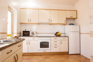 Eine Küche mit weißen Schränken, einer Mikrowelle, einem Backofen, einem Kühlschrank und einer Obstschale auf der Arbeitsplatte.