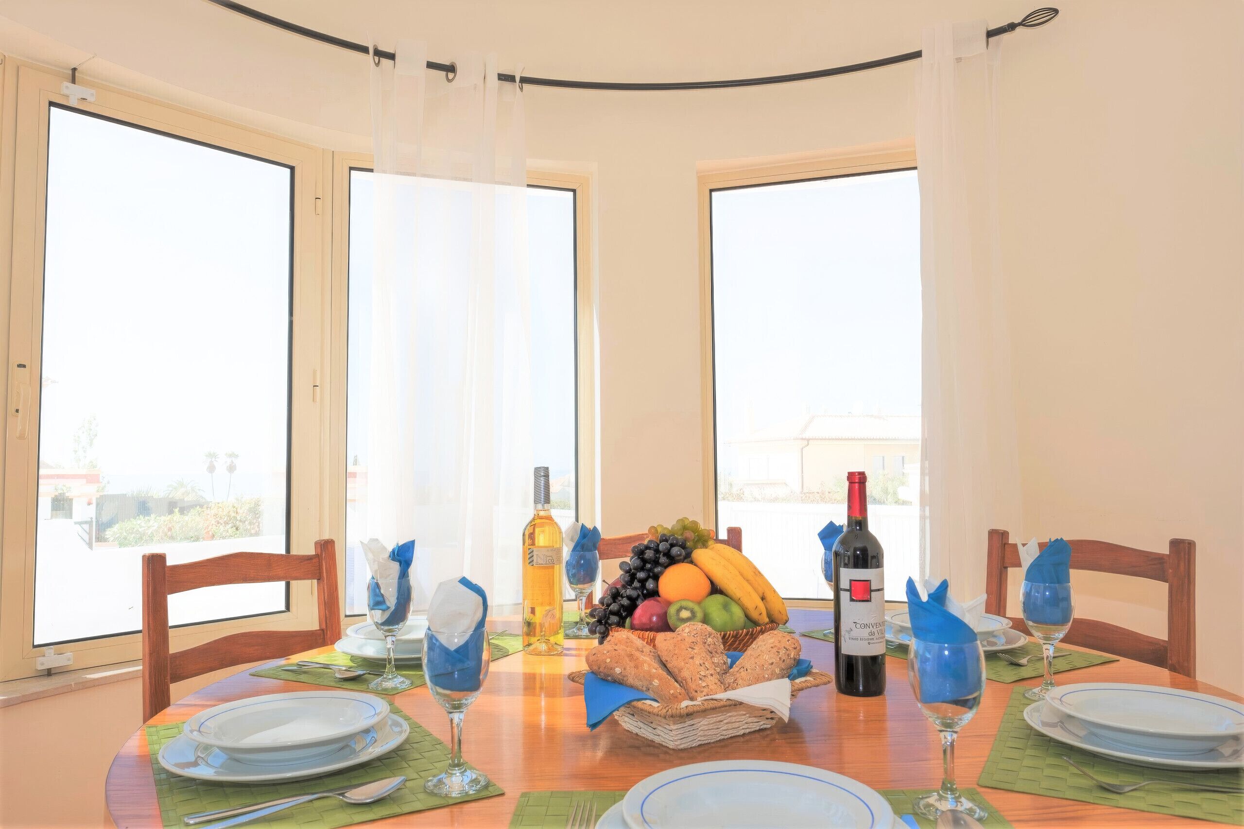 A dining table with plates, glasses, a bottle of wine, and a fruit basket.