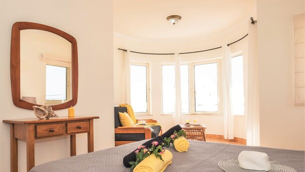 Une chambre à coucher avec un grand lit, une table de chevet, un miroir et une fenêtre avec des rideaux.