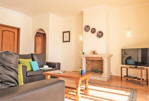 A living room with a sofa, a coffee table, a fireplace, and a television. - Villa w/ heatable pool & sea view in Galé (Albufeira)
