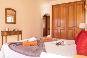 A hotel room with two beds, a wooden wardrobe, a mirror, a bedside table with a lamp, and a tray with snacks. - Villa w/ heatable pool & sea view in Galé (Albufeira)