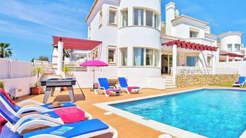En modern villa med en swimmingpool, solstolar och en täckt uteplats.