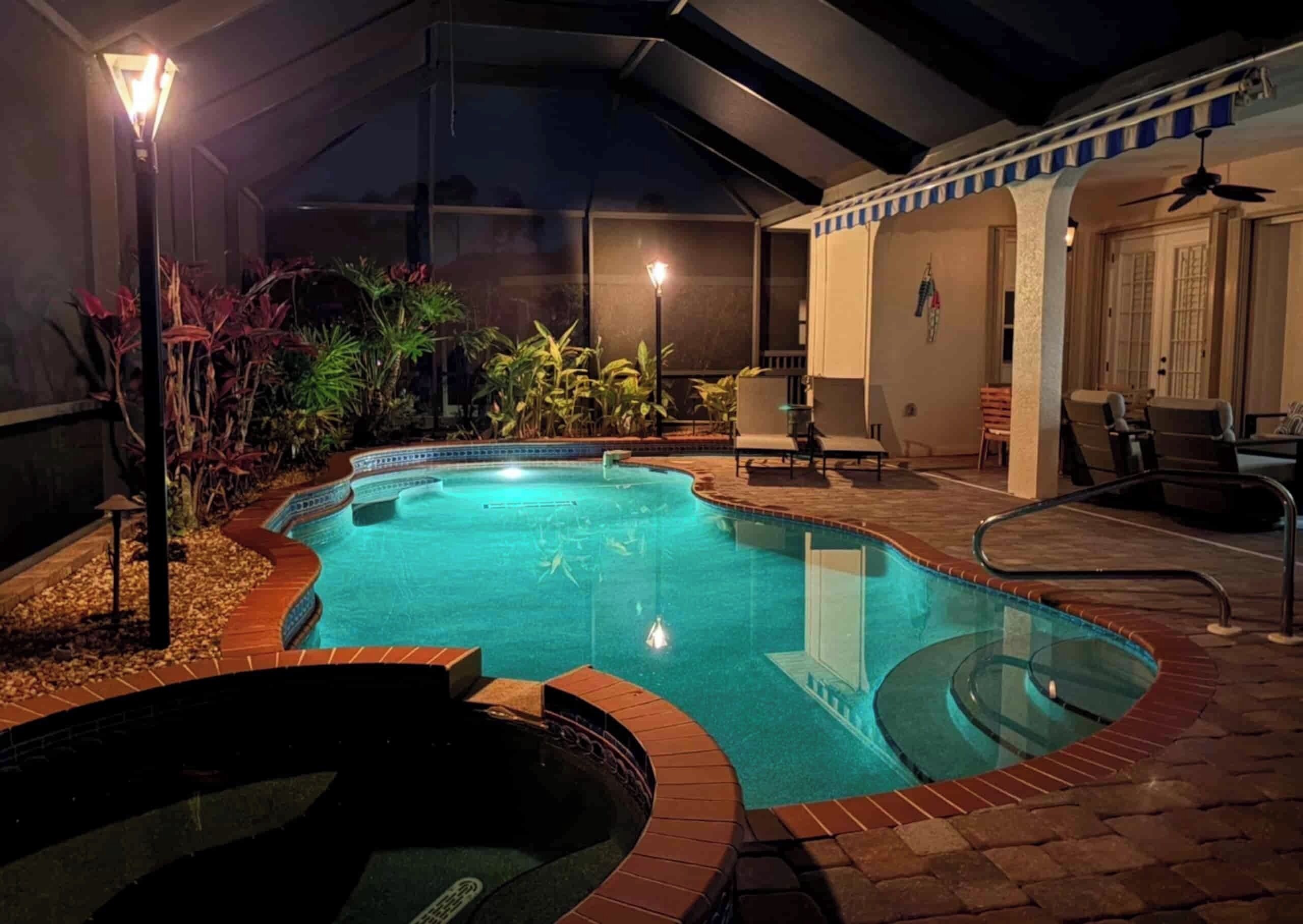 An outdoor swimming pool with a hot tub, surrounded by plants and outdoor furniture.