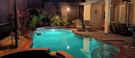 An outdoor swimming pool with a hot tub, surrounded by plants and outdoor furniture.