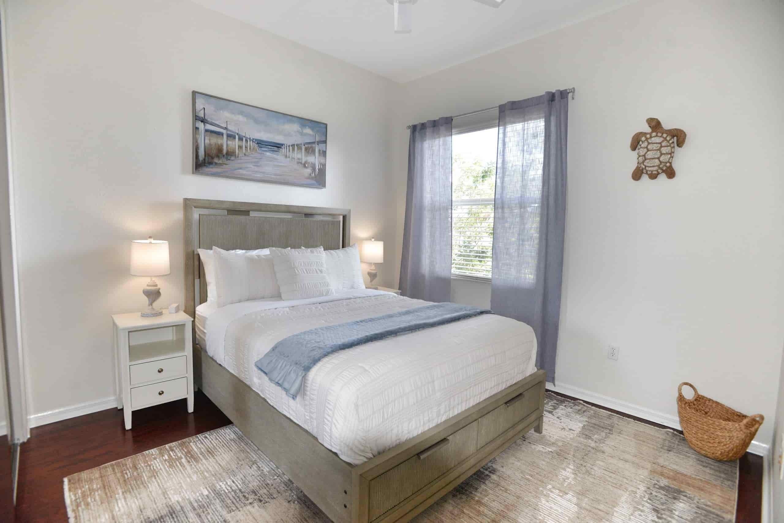 A bedroom with a bed, nightstands, a painting, a window with curtains, and a wall decoration.