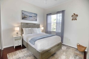 Un dormitorio con cama, mesitas de noche, un cuadro, una ventana con cortinas y un adorno en la pared.