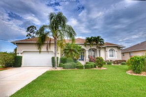 A two-story house with a garage, a well-maintained lawn, and a variety of shrubs and trees. - Perfect 4-bedroom house with heated pool in Rotonda West for large families! (Rotonda West)