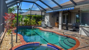 A swimming pool with a glass enclosure and a hot tub, surrounded by patio furniture and plants. - Perfect 4-bedroom house with heated pool in Rotonda West for large families! (Rotonda West)