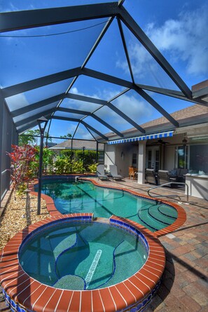 A swimming pool with a glass enclosure and a hot tub, surrounded by patio furniture and plants. - Perfect 4-bedroom house with heated pool in Rotonda West for large families! (Rotonda West)