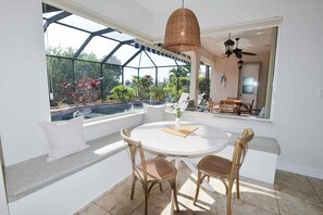 A sunlit room with a glass-enclosed patio, a round table with chairs, and a hanging light fixture. - Perfect 4-bedroom house with heated pool in Rotonda West for large families! (Rotonda West)