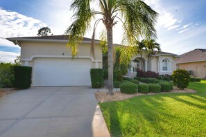 A single-story house with a garage, a well-maintained lawn, and a palm tree. - Perfect 4-bedroom house with heated pool in Rotonda West for large families! (Rotonda West)