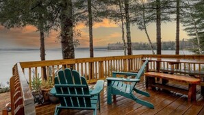 Een houten terras met Adirondack-stoelen en een picknicktafel, met uitzicht op een waterpartij.