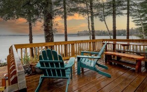 Eine Holzterrasse mit Adirondack-Stühlen und einem Picknicktisch mit Blick auf ein Gewässer.