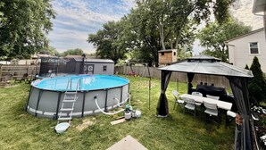A backyard with a swimming pool, a covered patio, and a fenced area.