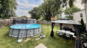 A backyard with a swimming pool, a covered patio, and a fenced area.
