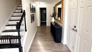 A hallway with a staircase, a light fixture, a mirror, and a door.
