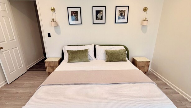 A bedroom with a large bed, two bedside tables, a door, and three wall-mounted picture frames.