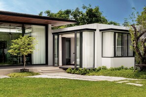 A modern house with a glass facade, a covered porch, and a well-maintained lawn. - Botanica Foresta Luxury 4BR Villa • Private Pool (Thep Krasatti)