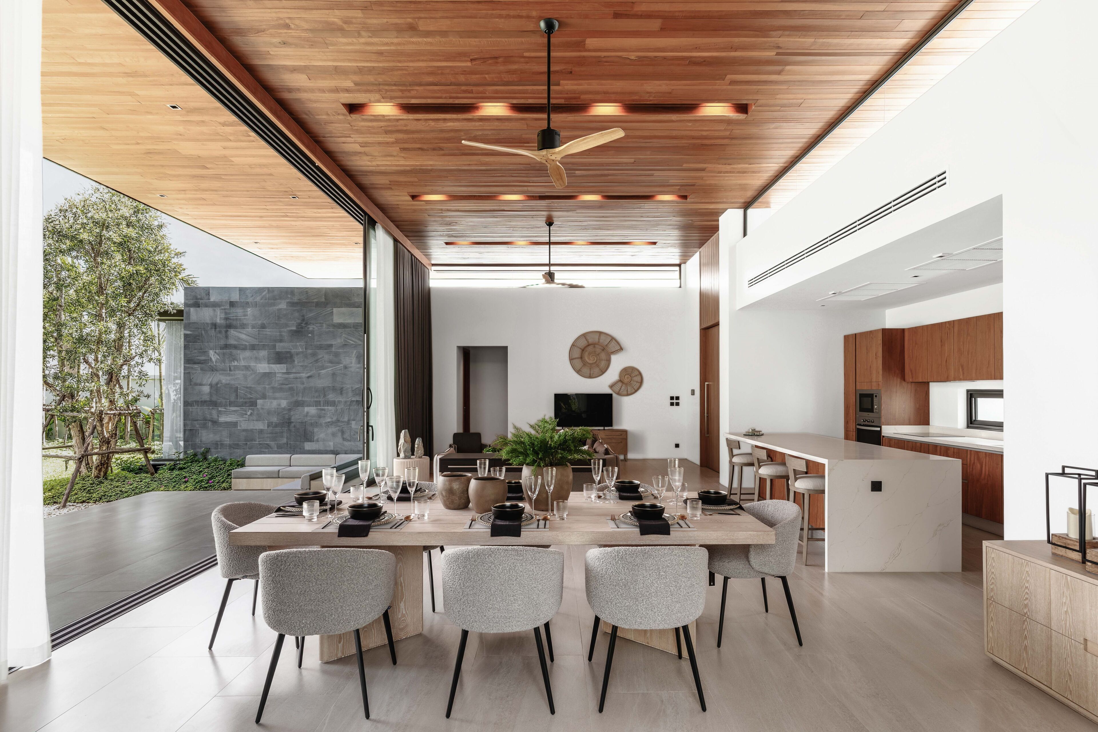 A modern dining area with a long table, grey upholstered chairs, and a ceiling fan.