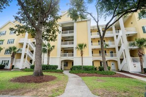 A multi-story building with balconies, a central walkway, and palm trees. - 2 bed 2 bath condo in Ocean Keyes, N. Myrtle Beach (North Myrtle Beach)