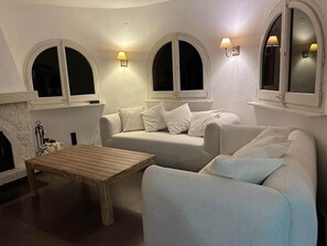 A cozy living room with a fireplace, a sofa, a coffee table, and two arched windows with wall-mounted lamps. - Stunning Villa in Sa Riera (Begur) (Sa Riera)
