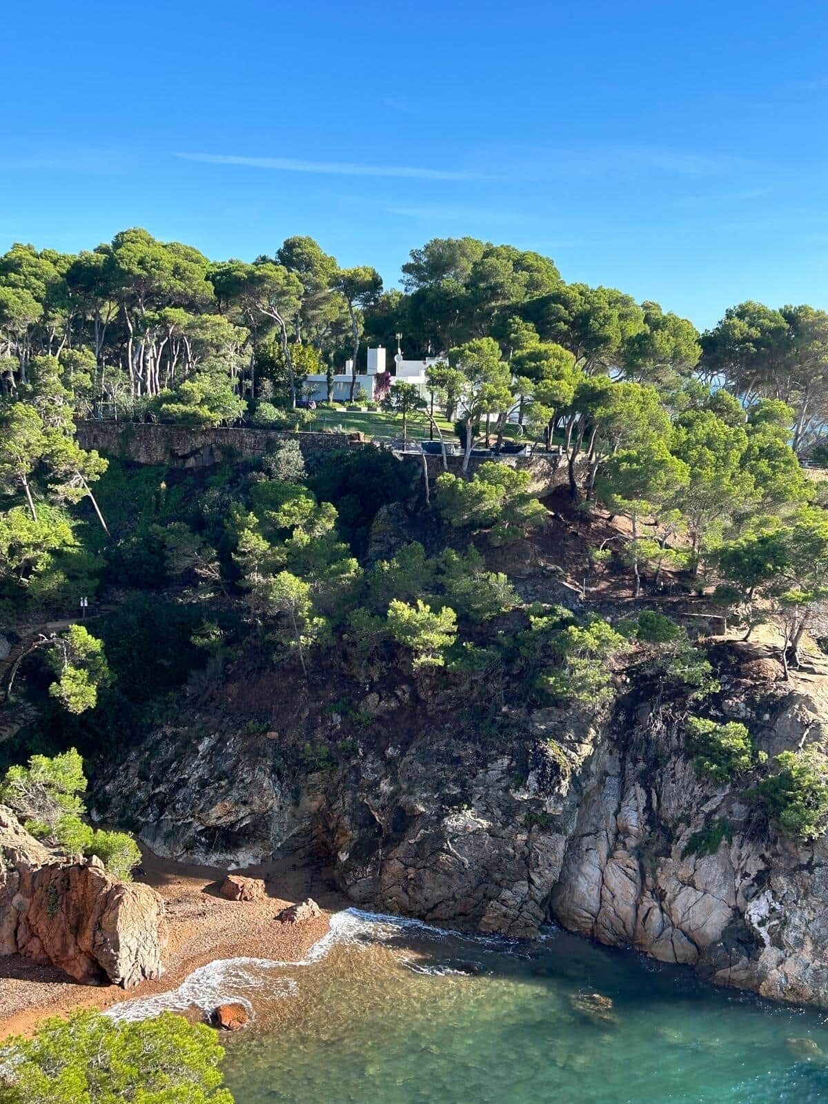 A coastal property with a rocky cliff, clear water, and dense greenery.
