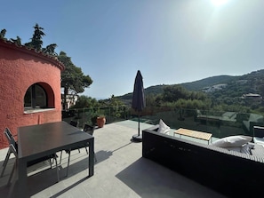 A rooftop terrace with a table, chairs, a sofa, and a glass balustrade overlooking a scenic landscape. - Stunning Villa in Sa Riera (Begur) (Sa Riera)
