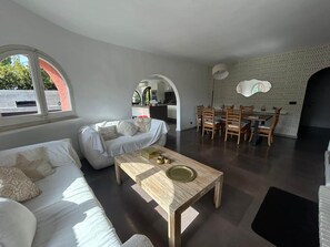 A modern living space with a sofa, coffee table, dining table with chairs, and a kitchen area visible through an archway. - Stunning Villa in Sa Riera (Begur) (Sa Riera)