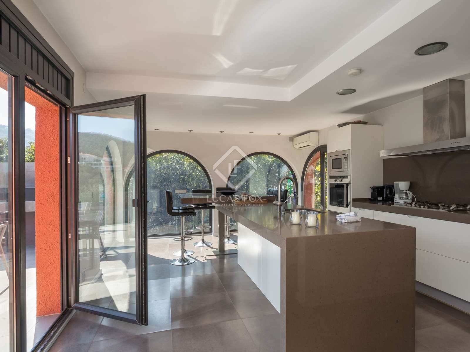 A modern kitchen with a central island, stainless steel appliances, and a glass door leading to an outdoor area.
