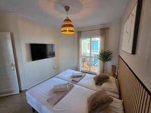 A hotel room with two beds, a television, a ceiling light, and a balcony with a view.