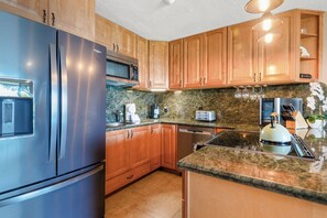 Eine moderne Küche mit Edelstahlgeräten, Holzschränken und Granit Arbeitsplatten, inklusive eingebautem Backofen.
