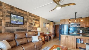 Ein modernes Wohnzimmer mit braunem Ledersofa, einem Holzes Esstisch und einer Küche mit Holzschränken und Edelstahlgeräten.