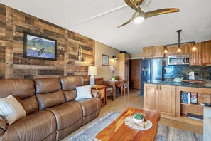 Ein modernes Wohnzimmer mit braunem Ledersofa, einem Holzes Esstisch und einer Küche mit Holzschränken und Edelstahlgeräten.