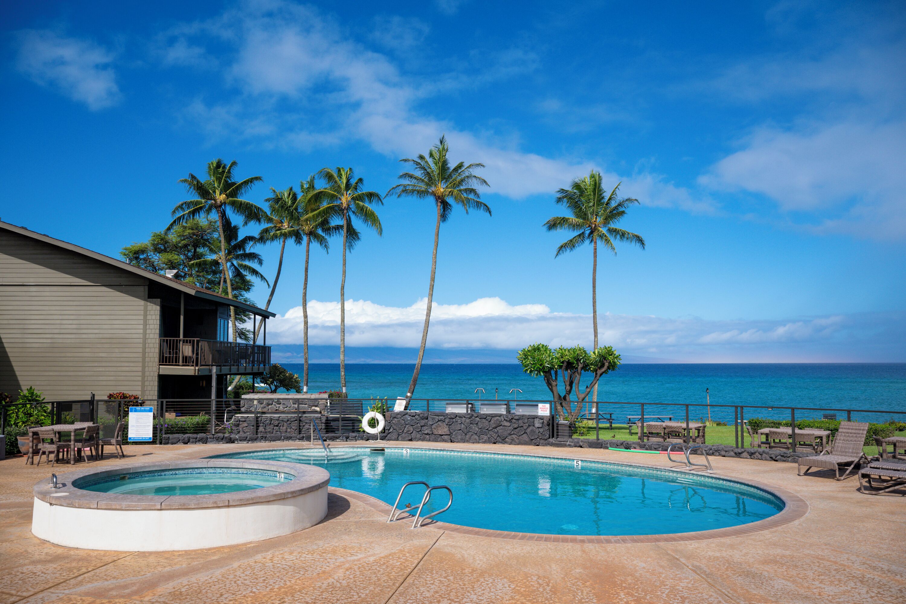 A pool area with a hot tub, lounge chairs, and a view of the ocean.