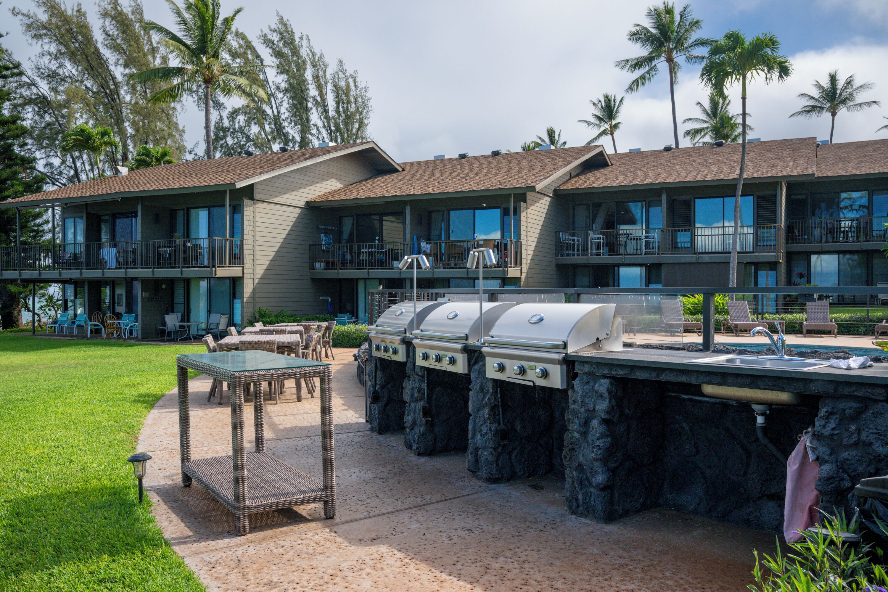 A hotel with outdoor grilling stations, a pool, and a well-maintained lawn.