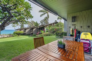 A wooden table with a potted plant, a beach view, and a house with a stone facade. - Polynesian Shores 114 by Gather - Oceanfront 1BR w/ Pool & Ocean Views (Lahaina)