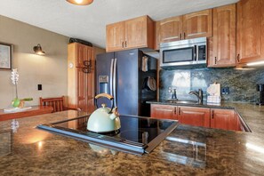 A kitchen with wooden cabinets, a stainless steel refrigerator, a microwave, and a kettle on the countertop. - Polynesian Shores 114 by Gather - Oceanfront 1BR w/ Pool & Ocean Views (Lahaina)
