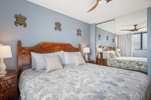 Ein Schlafzimmer mit einem großen Bett, zwei Nachttischen mit Lampen, einem Deckenventilator und einem großen Spiegel, der den Raum widerspiegelt.