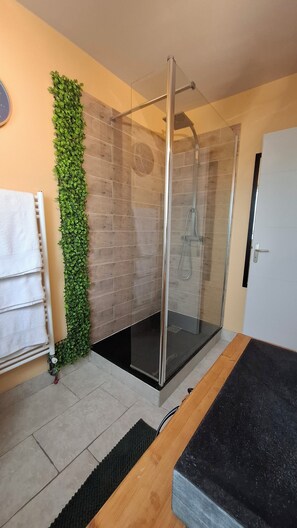 A modern bathroom with a glass-enclosed shower, a green wall decoration, a towel rack, and a wooden bench. - Charming house with an enclosed garden and a patio between Chartres and Rambouillet (Auneau)