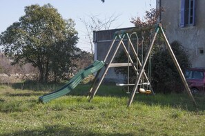 A swing set with a slide in a grassy area with a building in the background. - Domaine Mas Pigné: 6-Bedroom House (Sauve)