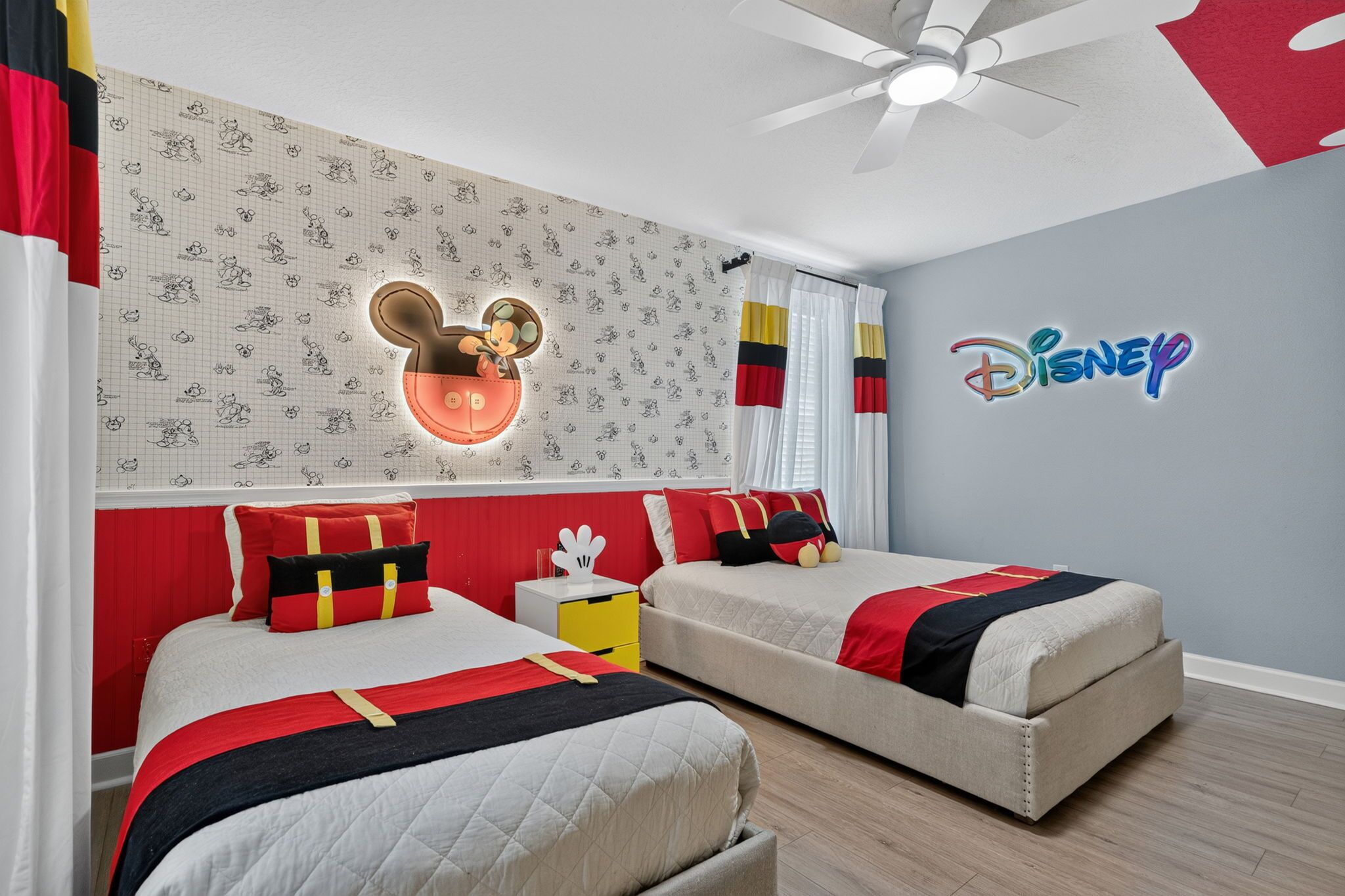 Ein Hotelzimmer mit zwei Betten, einer Mickey-Mouse-Lampe und dem Disney-Logo an der Wand.