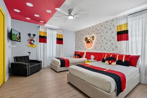 Ein Schlafzimmer mit zwei Betten, einem Deckenventilator, Wanddekoration mit Mickey Mouse und einem Fernseher.