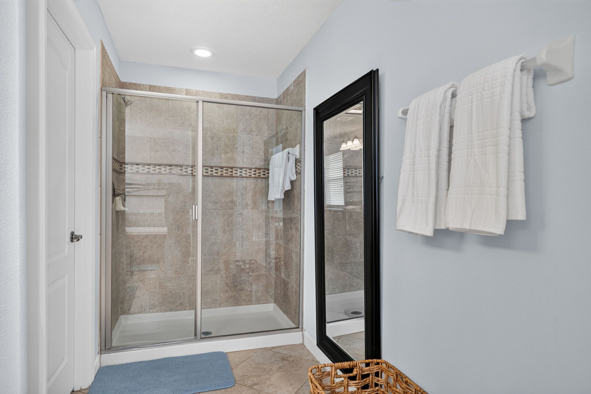 Une salle de bain avec une douche à parois de verre, un porte-serviettes blanc et un tapis de bain bleu.