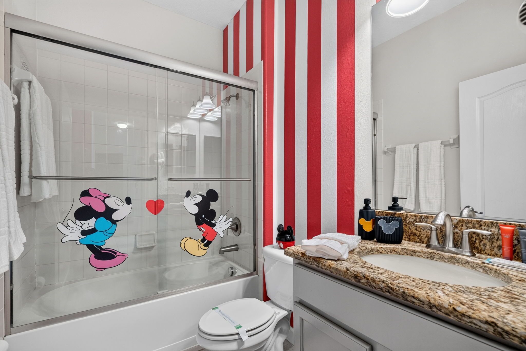 Een badkamer met Mickey Mouse stickers, een douche, toilet en een wastafel met spiegel.
