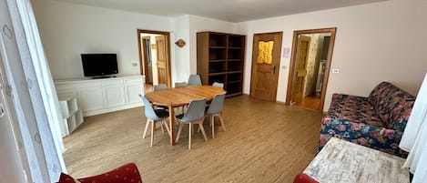 A living room with a wooden dining table, two sofas, a TV, and a bookshelf.