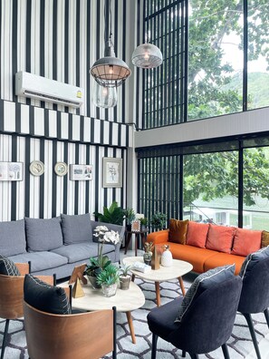 A modern interior with striped walls, a sofa, chairs, a coffee table, and a window with a view of greenery.